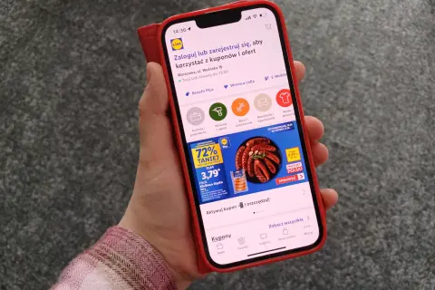Dłoń trzymająca smartfon z aplikacją Lidl Plus, na ekranie widoczna promocja na kiełbasę.