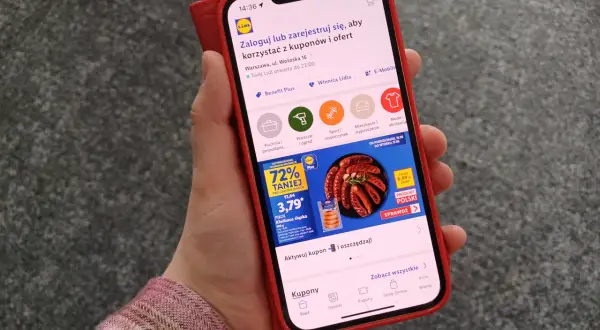 Dłoń trzymająca smartfon z aplikacją Lidl Plus, na ekranie widoczna promocja na kiełbasę.